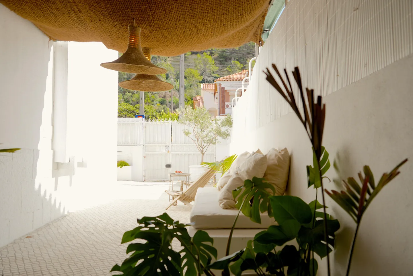 Covered patio with a built-in bench, a white mattress, light cushions and wooden deck chairs